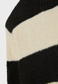 Pull en maille épaisse à rayures crème et noires, avec un col rond et des poignets côtelés, doté d'une finition douce et texturée.