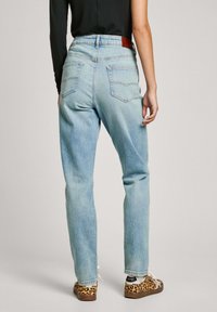 Lichtblauwe denim jeans met een rechte pasvorm, hoge taille en twee achterzakken. Draagt een paar sneakers met luipaardprint.