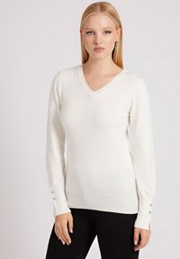 Maglione bianco a V con maniche lunghe, polsini a coste con tre bottoni argentati, realizzato in un tessuto morbido, design aderente. Pantaloni neri.