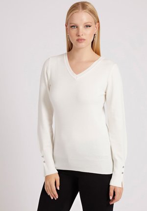 Maglione bianco a V con maniche lunghe, polsini a coste con tre bottoni argentati, realizzato in un tessuto morbido, design aderente. Pantaloni neri.