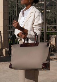 Grote beige tote bag met bruin krokodillenprint leren accenten en handvatten. Glad materiaal met een gestructureerde vorm en subtiele hardwaredetails.