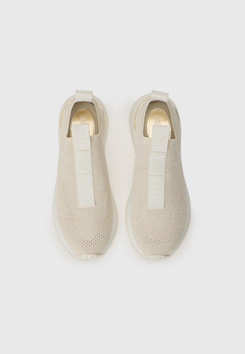 Beige gebreide instapschoenen met een gestructureerd oppervlak, voorzien van een opvallende witte logotab en een gladde, lichtgekleurde zool.