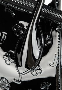 Czarna torba typu tote z lakierowanej skóry, zdobiona wytłoczonymi kwiatowymi wzorami i zamkiem błyskawicznym u góry. Gładka faktura z kontrastującymi przeszyciami i detalami uchwytów.