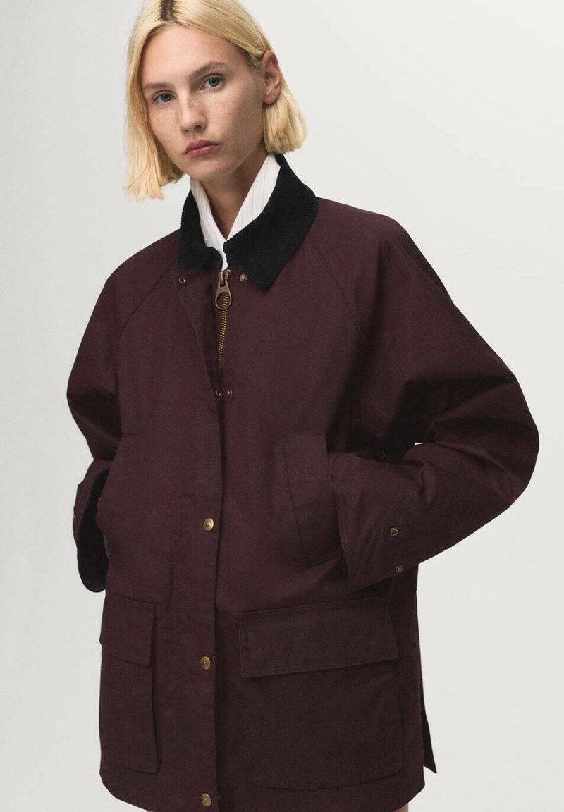 Chaqueta burdeos con cuello de pana, cremallera dorada y bolsillos frontales. Ajuste casual, textura suave y detalles de botones en los puños.