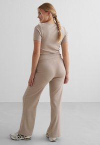 Beige ribbet striktrøje med korte ærmer parret med fitted beige bukser. Outfittet har et behageligt, afslappet design med en glat tekstur.
