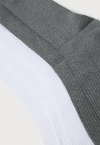 Stak af ribbede ankelstrømper, hvid og grå, lagt fladt på en lys overflade, der viser tekstur og detaljer ved skaftet.