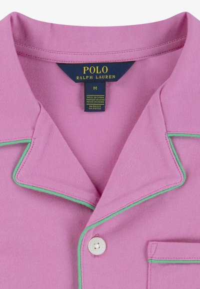 Lila polo skjorta med grön kant längs kragen och fickan, en enkel knappstängning och en etikett som säger "POLO RALPH LAUREN."