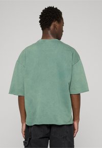 T-shirt vert surdimensionné en tissu texturé, avec un col rond et des manches courtes, présentant une finition légèrement usée à l'ourlet.