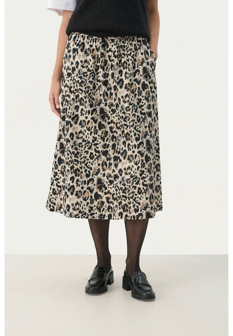 Jupe midi en imprimé léopard en tissu doux, dotée d'une taille élastique et de poches latérales. Associée à des mocassins noirs et des collants noirs transparents.