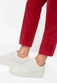 Weiße Leder-Sneaker mit glatter Oberfläche und fünf Ösen, kombiniert mit roten Cordhosen mit gerippter Textur und verkürzter Länge.