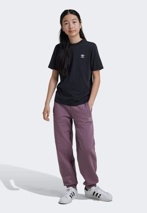 Sort bomuld t-shirt med hvidt logo, parret med afslappede lyserøde sweatpants med logo, båret med hvide sko med sorte striber.