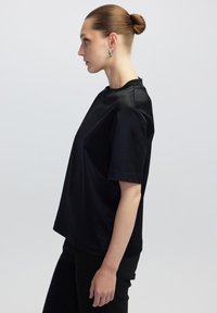 Camiseta negra de manga corta en tejido suave, con cuello redondo y corte relajado, combinada con pantalones negros.