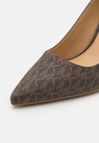 Pompe à talon aigu en tissu brun avec un motif texturé. Doublure intérieure lisse beige. Talon légèrement effilé et silhouette élégante.