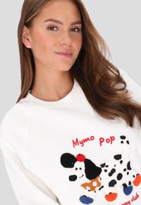 Sudadera blanca con un gráfico bordado colorido de un perro, con acentos en rojo y negro. Modelo luciendo pendientes divertidos a juego.