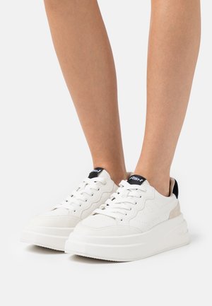 Weiße Ledersneaker mit einer dicken Plattformsohle, perforierten Details und einem beigen Wildlederakzent an der Ferse. Schwarzes Logo auf der Zunge.