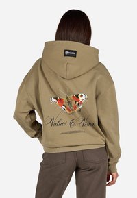 Khaki-Hoodie mit einem Rücken-Butterfly-Graphic in lebhaftem Rot, Schwarz und Weiß, darunter der Text "Werte & Vision". Weicher, lässiger Schnitt.