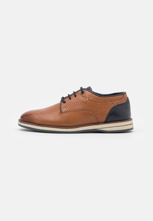 Chaussure à lacets pour homme en cuir marron avec côtés perforés et talon bleu marine foncé, semelle crème avec dessous noir, vue de côté sur fond blanc.