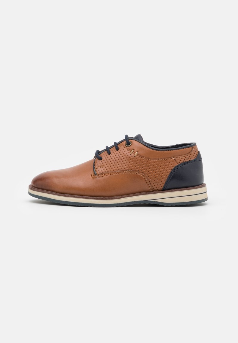 Chaussure à lacets pour homme en cuir marron avec côtés perforés et talon bleu marine foncé, semelle crème avec dessous noir, vue de côté sur fond blanc.