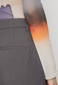 Pantaloni grigi fitted con un dettaglio sulla tasca posteriore, abbinati a una maglietta a maniche lunghe con un design a gradiente nelle tonalità pesca e viola.