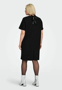 Czarna sukienka z krótkim rękawem o luźnym kroju, z dekoltem typu keyhole z tyłu, zawiązana czarną satynową kokardą. Noszona z błyszczącymi srebrnymi botkami.