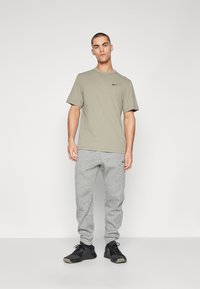 Nike oliiviroheline puuvillane T-särk, millele on sobitatud hallid dressipüksid ja mustad sportjalatsid. Särgil on väike must logo.