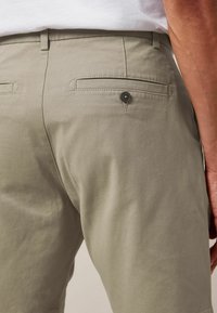 Pantaloni verde oliva chiaro con tasca posteriore con bottone, tessuto dalla texture liscia, vestibilità sartoriale e dettagli di cuciture sottili.
