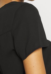 Top nero a maniche corte con vestibilità rilassata, texture morbida e cuciture visibili sulle spalle. Design semplice con taglio classico.