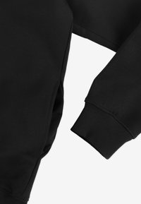 Czarna bluza z prążkowanymi mankietami i teksturowaną powierzchnią, o luźnym kroju i z detalem bocznej wstawki.