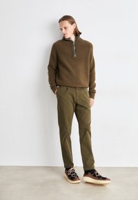 Pull à mailles brunes texturé avec col zippé, pantalon tapered vert olive, et baskets noires et brunes à motif avec semelles crème.