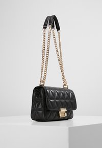 Černá kožená kabelka s prošívaným vzorem kosočtverců, zlatým řetízkovým uchem a kovovými doplňky, obdélníkového tvaru a s klopovým zapínáním.