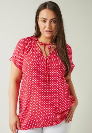 Blusa roja con lunares blancos, de manga corta, escote en V, detalle de lazo en el cuello y un corte relajado. Textura de tela suave.