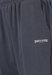 Marineblaue Sweatpants aus Baumwolle, ausgestattet mit einem elastischen Bund, Seitentaschen und einem bedruckten "SPORTS STUDIO" Logo in Weiß am Oberschenkel.