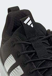 Čierna atletická obuv s okrajom z textilu, polstrovaným golierom a tromi bielymi pruhmi na boku. Obsahuje textúrované šnúrky a ucho na ťahanie.