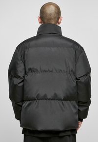 Jachetă puffer neagră, umplutură groasă, guler înalt, textură netedă, formă pătrată, acoperire completă, fără închideri sau modele vizibile.