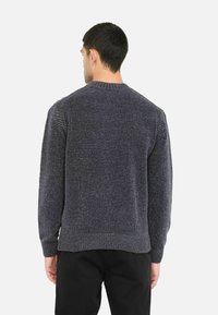 Sivi pleteni pulover s rebrastim manžetama i rubom, koji se odlikuje teksturiranom tkaninom i okruglom izrezom. Vidljive šavove na ramenima dodaju detalj.