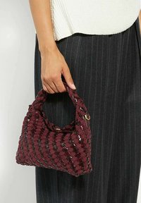 Woven burgundy handbag with a textured surface, short handle, and glossy accents. Compact shape with a structured design.