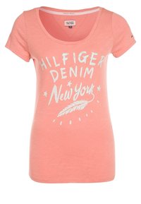 Camiseta de algodón rosa claro con escote de pico y mangas cortas. Presenta texto impreso en blanco: "HILFIGER DENIM Nueva York" y un gráfico de pluma.