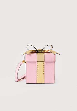 Small pink box-shaped handbag with a shiny gold vertical strap and bow on top, featuring a pink wrist strap on the side.
