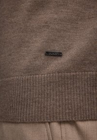 Brauner, gestrickter Pullover mit geripptem Saum und Manschetten. Hat ein kleines schwarzes Metall-Logo-Tag. Weicher Stoff und taillierte Passform.