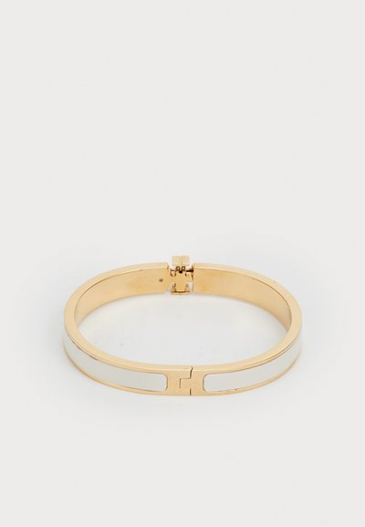 Bratara bangle din metal aurit, cu un inlay de email alb neted, având un sistem de închidere cu balama și un design geometric simplu.