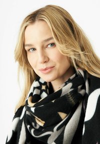 Zwart- en crèmekleurige sjaal met geometrische en bloemmotieven, gemaakt van zacht materiaal, losjes om de nek gewikkeld.