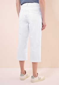 Vita cropped jeans med en avslappnad passform, med hög midja, två bakfickor och uppvikta fållar, i kombination med beige och gröna sneakers.