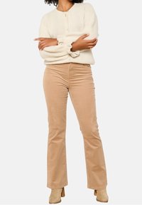 Beige kordfläktade byxor med subtil textur, kombinerade med en vit stickad cardigan med rund halsringning och knappstängning.