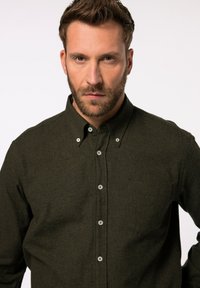 Camisa de color verde oscuro, abotonada, hecha de un tejido texturizado, con cuello, mangas largas y un bolsillo en el pecho; cuenta con botones plateados.