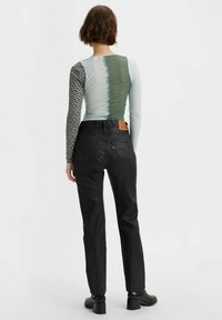 Långärmad topp med blandade mönster i nyanser av svart, grön och blå; kombinerad med höga svarta jeans och stövlar med blockklack.