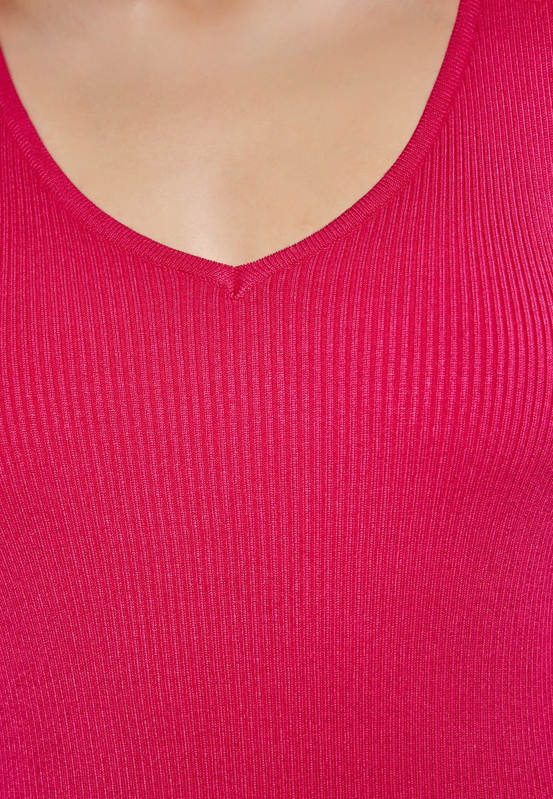 Tætsiddende, ribbet tanktop i lys pink med V-hals, der fremviser en glat tekstur og en subtil glans. Ideel til lag-på-lag eller afslappet brug.