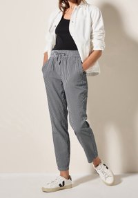 Pantalons à rayures noirs et blancs avec une taille élastique, des poches avant et des jambes fuselées, associés à une veste blanche et des baskets.