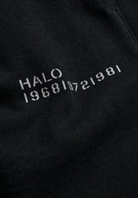 Schwarzer Stoff mit weißem Drucktext "HALO 1968 1972 1981", mit glatter Textur und minimalistischem Design.