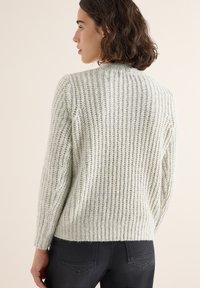 Hellgrüner Strickpullover mit geripptem Muster, langen Ärmeln, rundem Ausschnitt und lockerer Passform, kombiniert mit dunkelgrauen Hosen.
