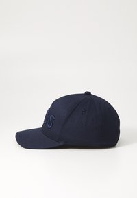 Mørkeblå caps med en strukturert form og flat brem. Har et brodert logo på fronten og stikkingdetaljer på kronen.